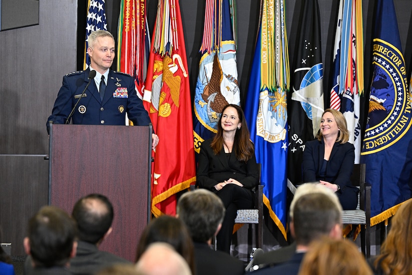 A man in uniform speaks from a podium as others watch.